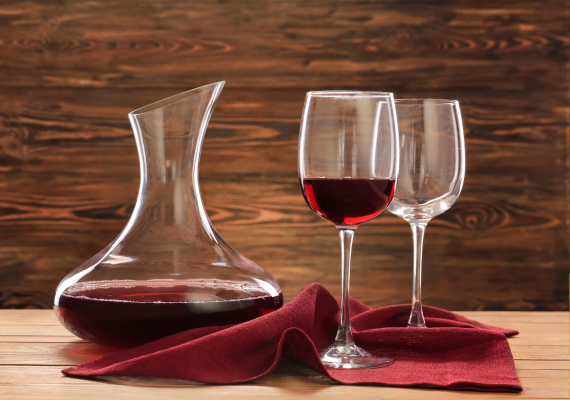 A decanter of red wine and two glasses, one of which is filled with red wine and one of which is empty.